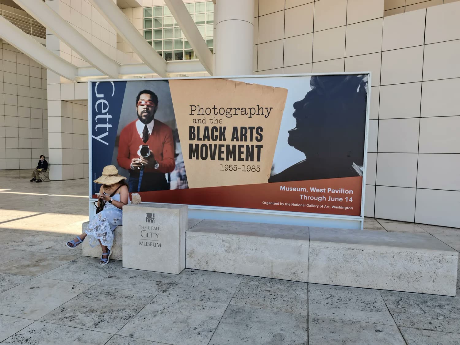 Jilly sitting beside an exhibition banner at the Getty Center.